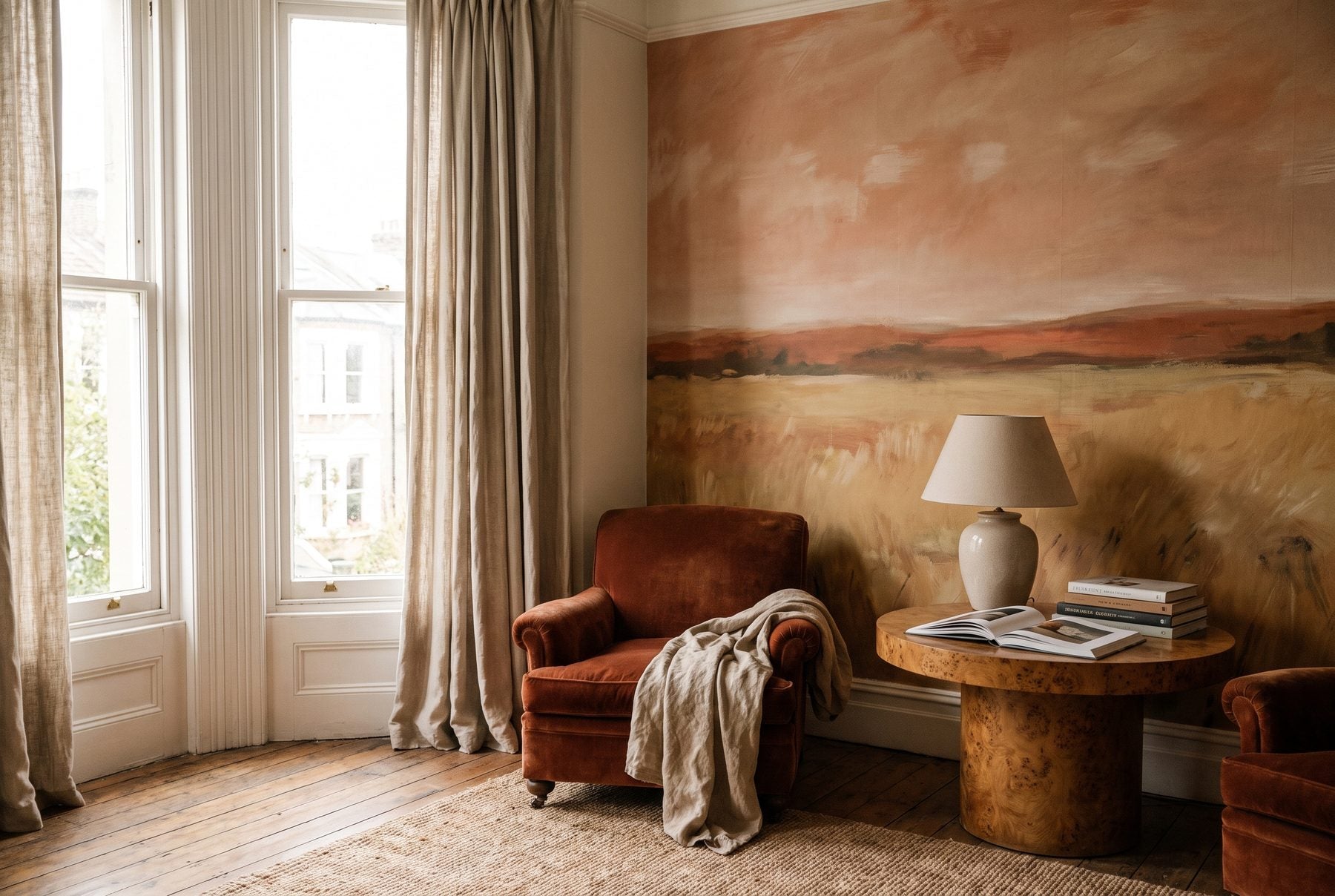 A painterly landscape mural in warm earth tones in a sunlit sitting room